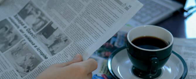 a person reading a newspaper with a cup of coffee