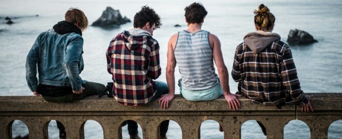 four person sitting on bench in front of body of water